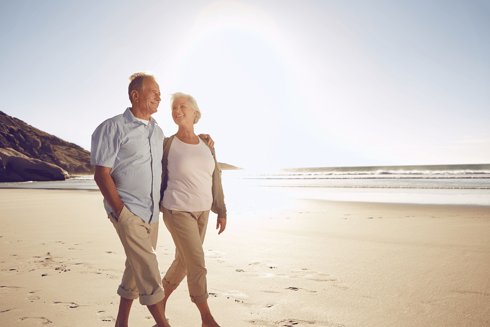 Elderly couple walking along a beach on a sunny day.